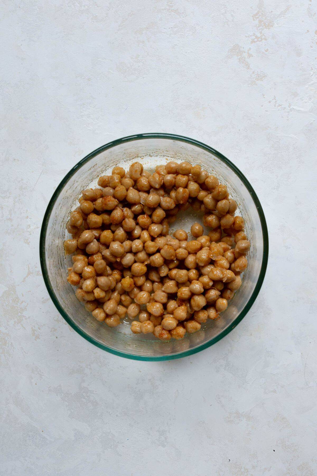 Seasoned chickpeas in a bowl before air frying, tossed with olive oil, garlic powder, paprika, onion powder, and salt.