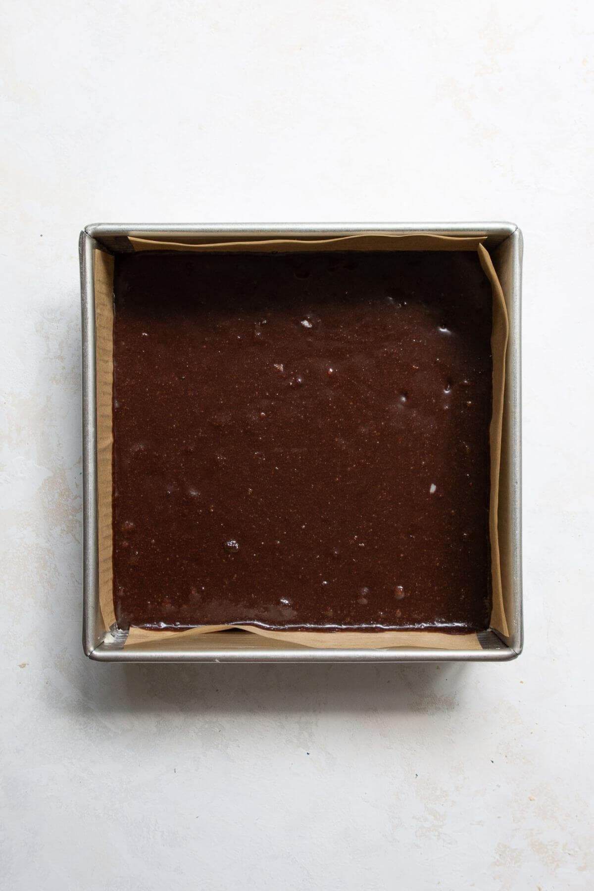 Healthy brownie batter in a lined baking pan before baking.
