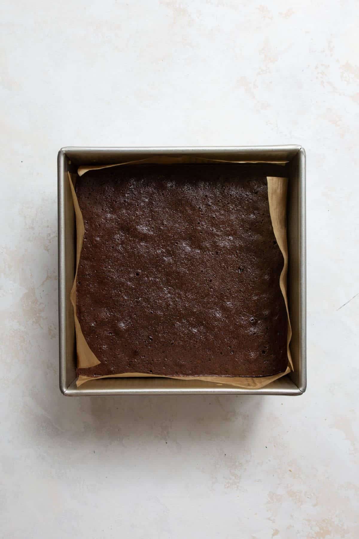 Baked fudgy almond flour brownies in a parchment-lined baking pan, fresh from the oven.