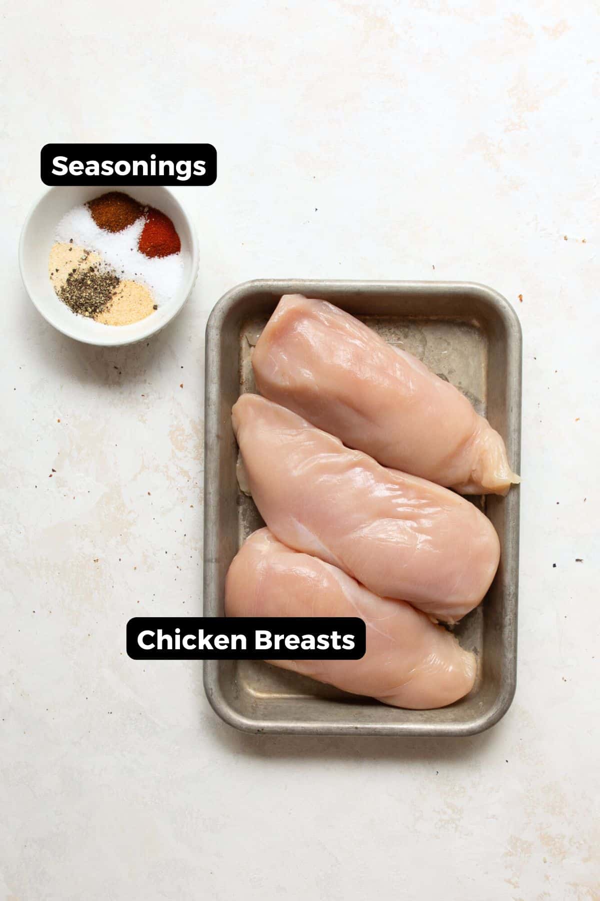 All ingredients in small bowls labeled including: chicken breast, garlic powder, onion powder, paprika, olive oil, fresh lemon, and parsley.