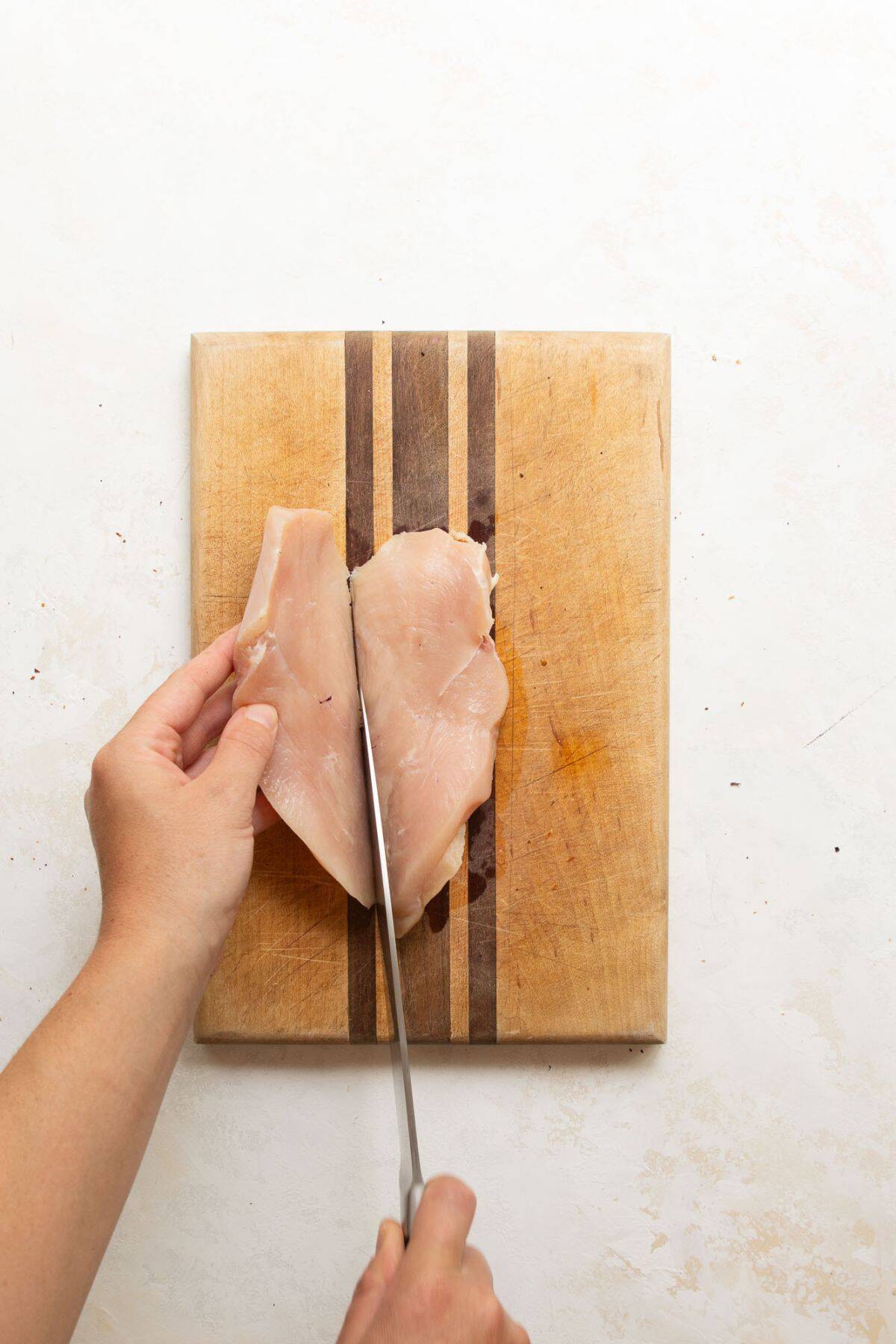 Cutting a boneless, skinless chicken breast in half horizontally to create thin, even slices for quick cooking.