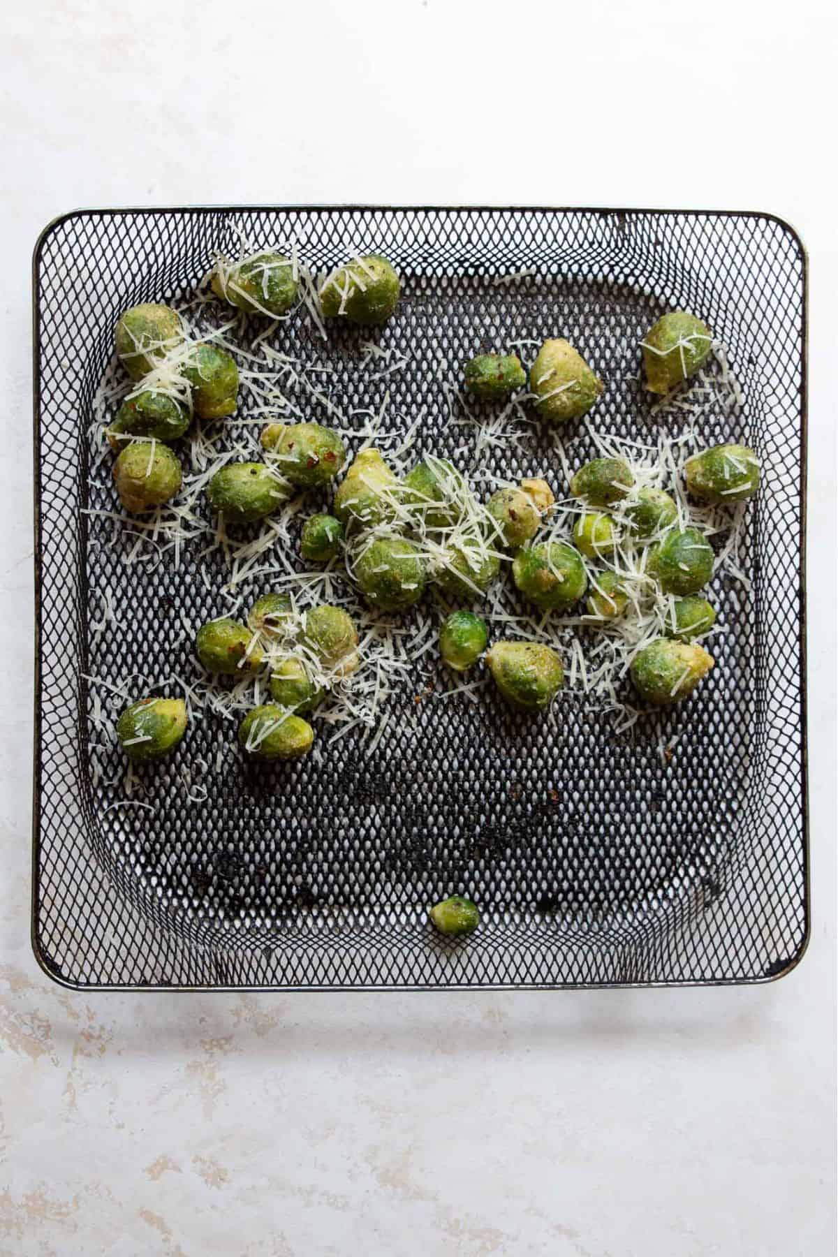 Sprinkling parmesan cheese on top of air fryer frozen Brussel in air fryer basket.