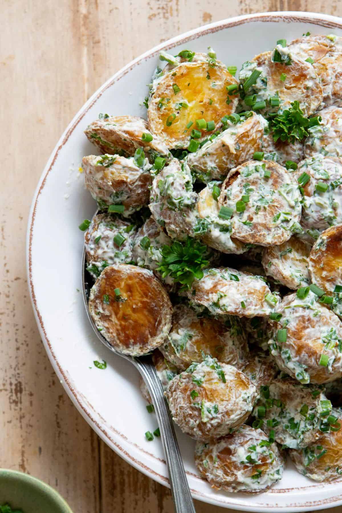 Bowl of crispy potato salad with golden roasted Yukon Gold potatoes tossed in a tangy Greek yogurt herb dressing, garnished with fresh parsley and chives.