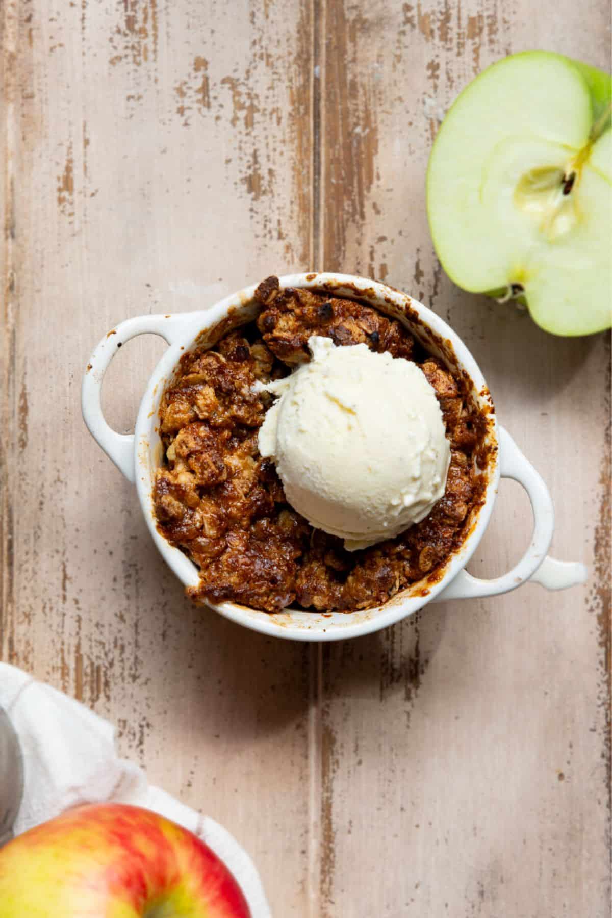 Healthy air fryer apple crisp in a single-serve ramekin with warm apples, a golden oat crumble topping, and a scoop of vanilla ice cream.