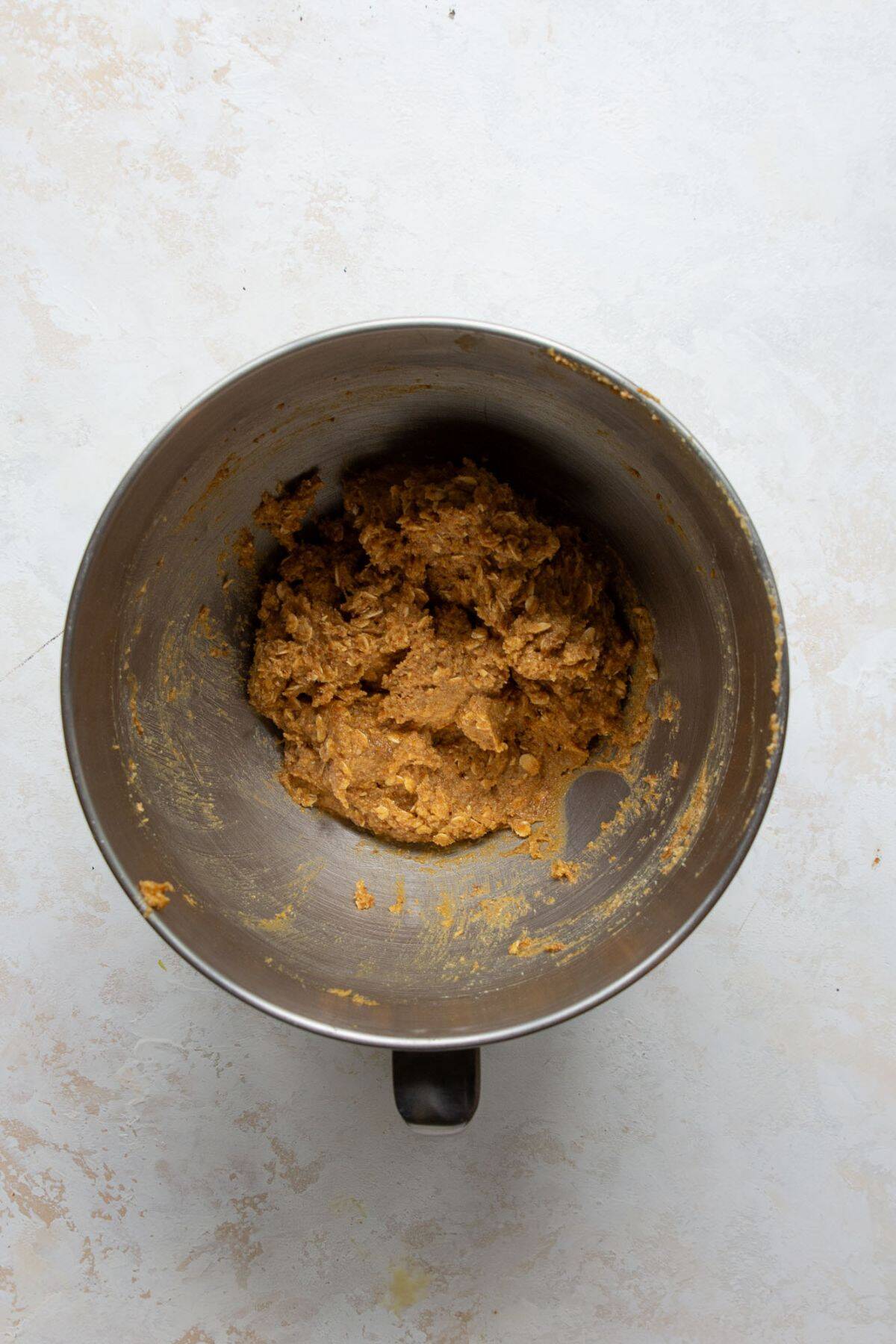 Adding almond flour, oats, baking soda, and salt to wet ingredients in a mixing bowl for cowboy pretzel cookies.