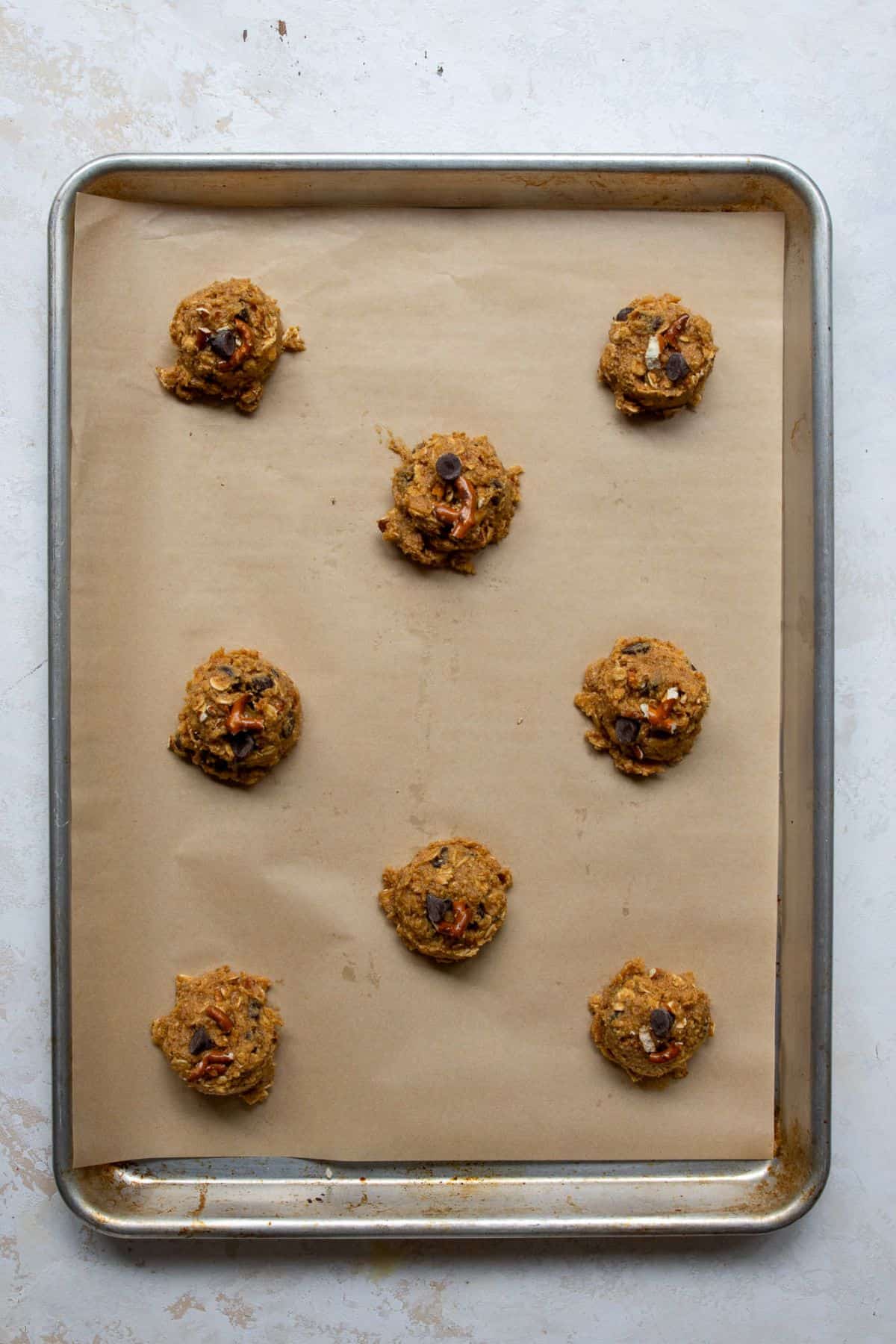 Unbaked cowboy pretzel cookie dough balls on a parchment-lined baking sheet.
