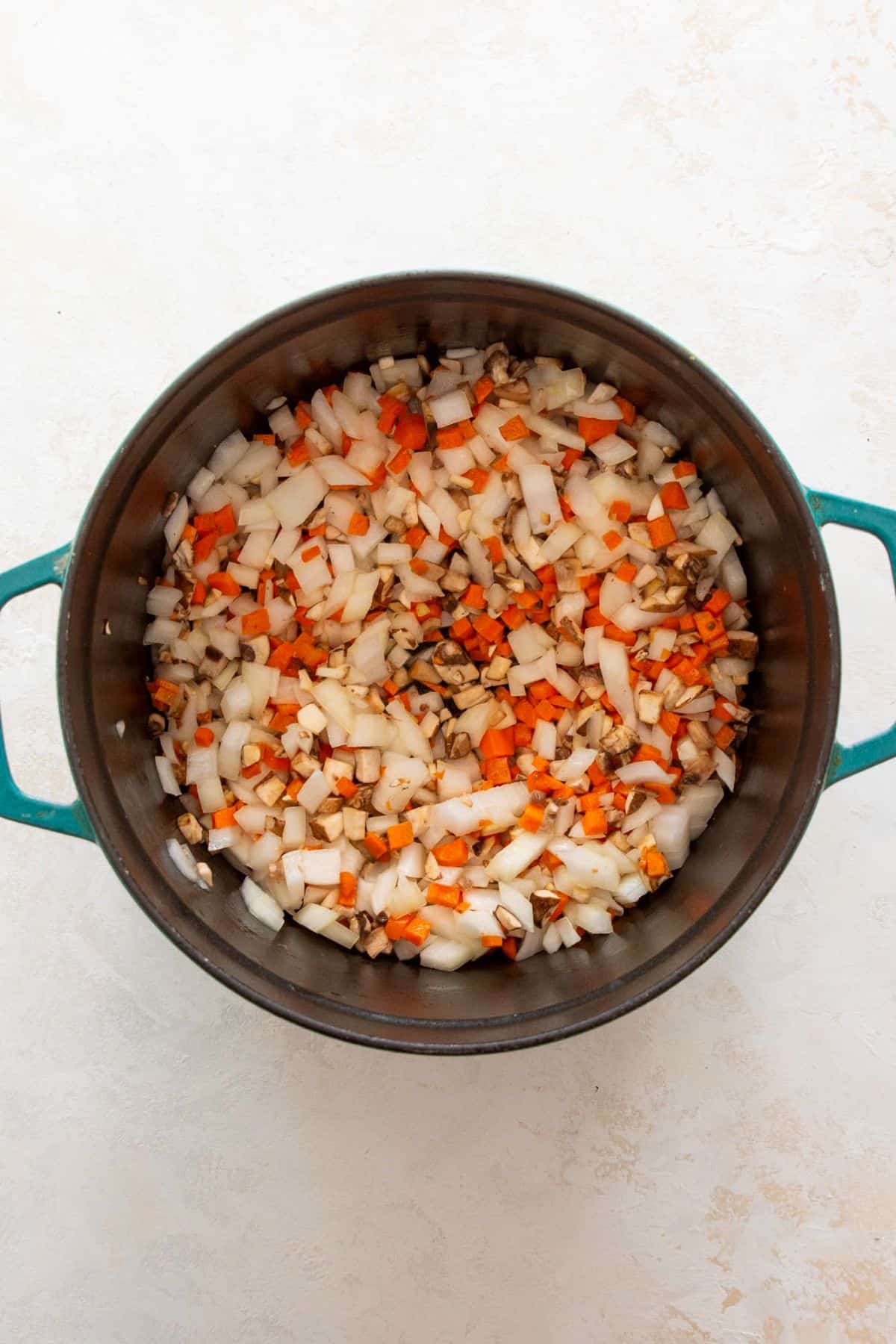 Adding diced carrots, onions, mushrooms, and garlic to a pot with olive oil to start the chicken bolognese base.