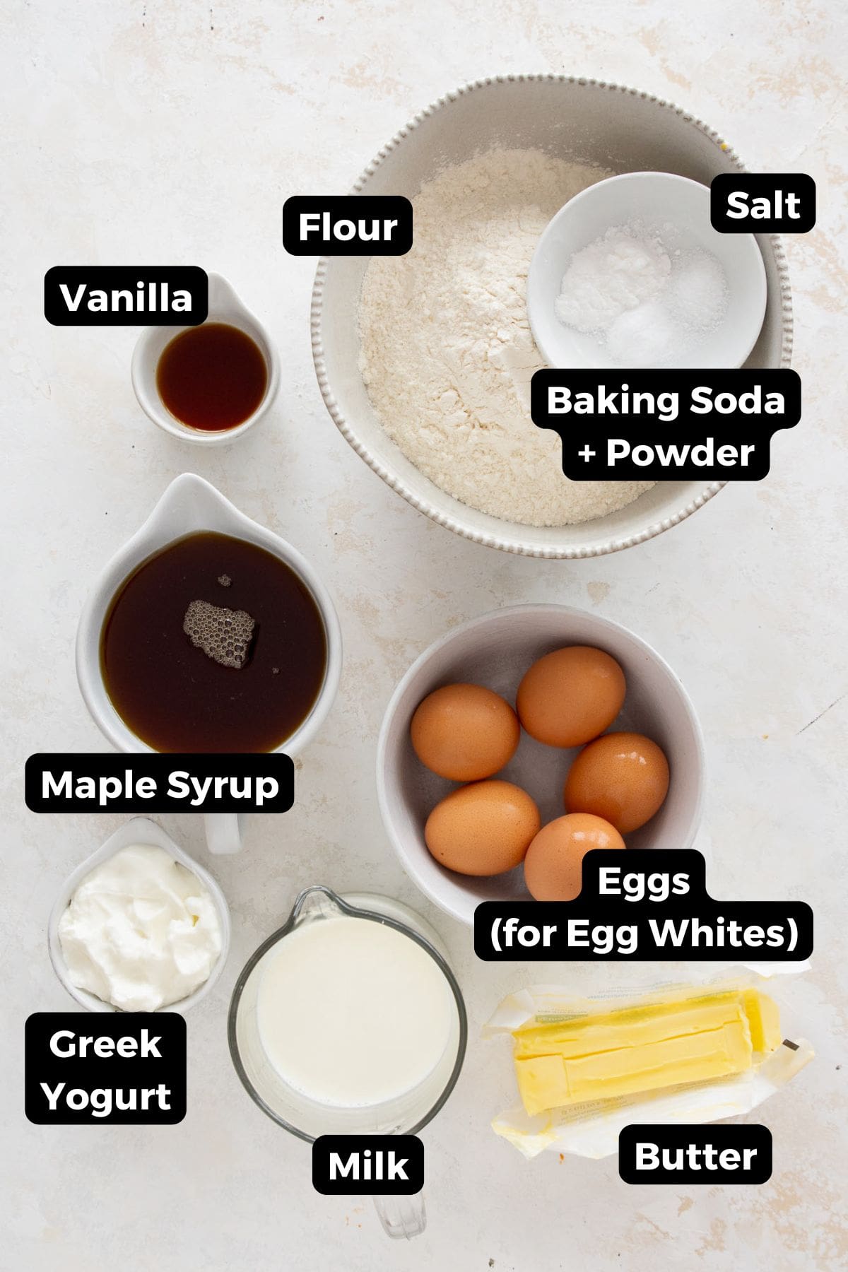 All ingredients for healthy vanilla birthday cake in labeled bowls — flour, Greek yogurt, maple syrup, egg whites, butter, baking powder, vanilla extract, and salt.