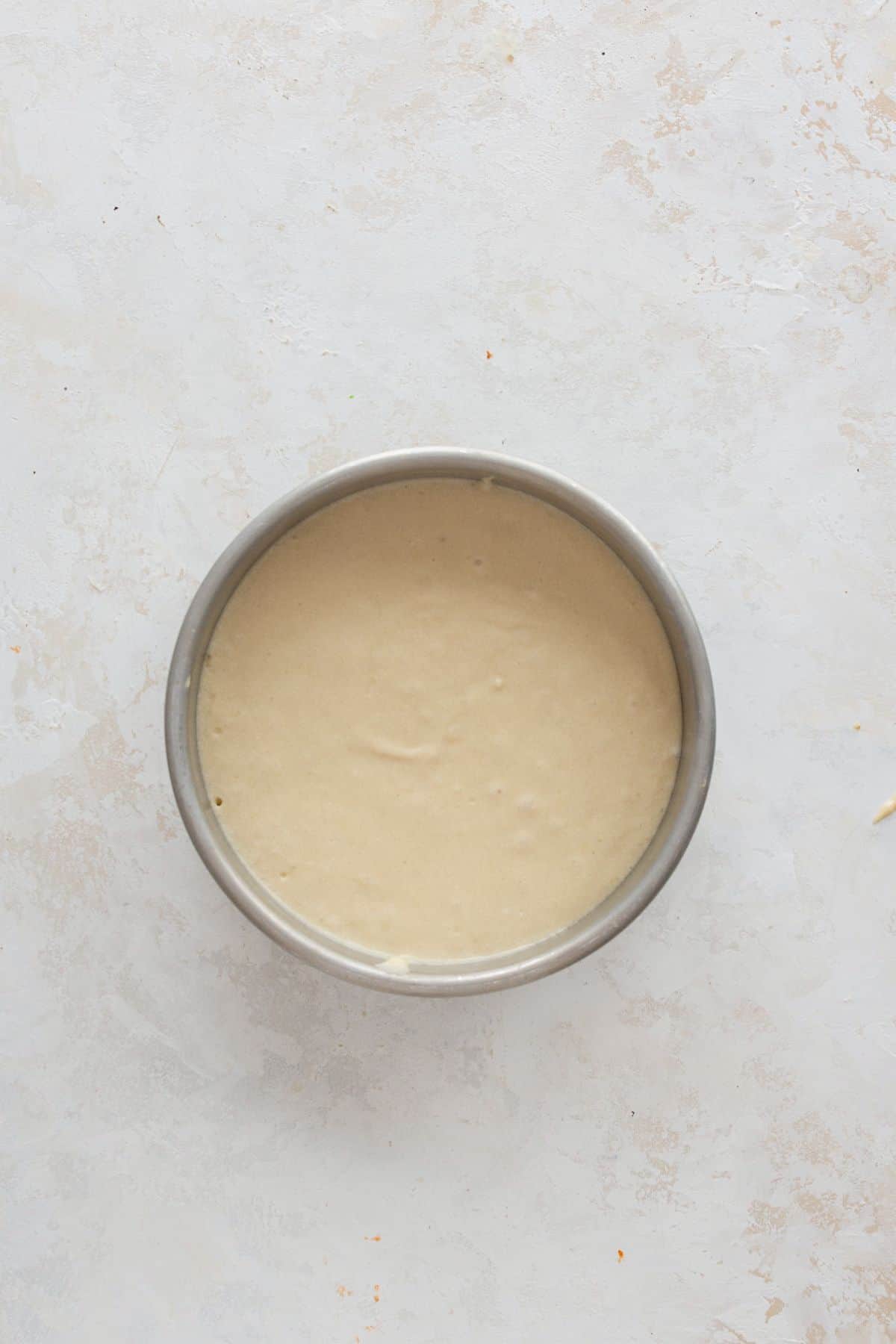 Pouring cake batter evenly into two parchment-lined round pans ready for baking.