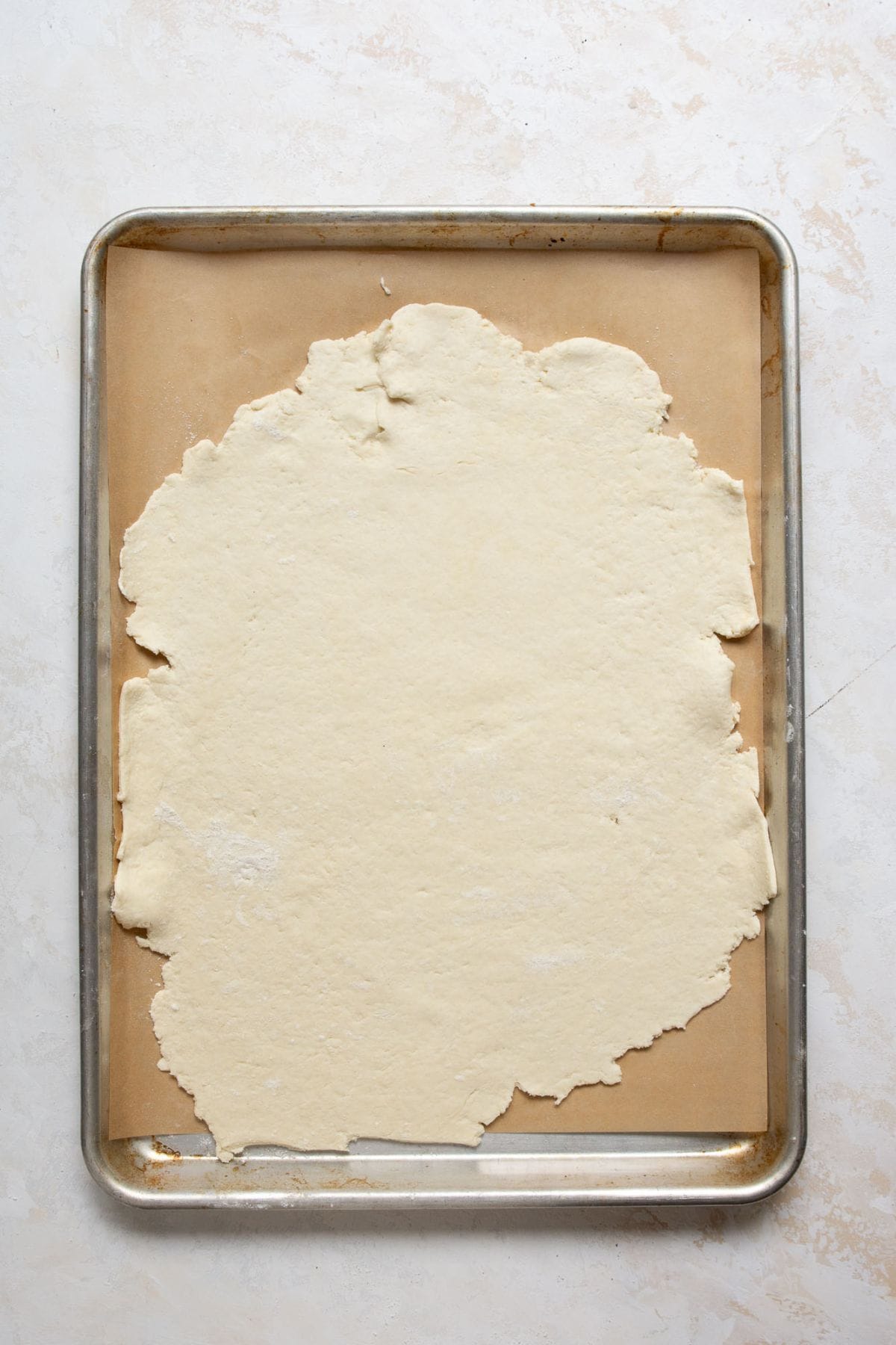 Thin Greek Yogurt Pizza Dough rolled out on a parchment-lined baking sheet.
