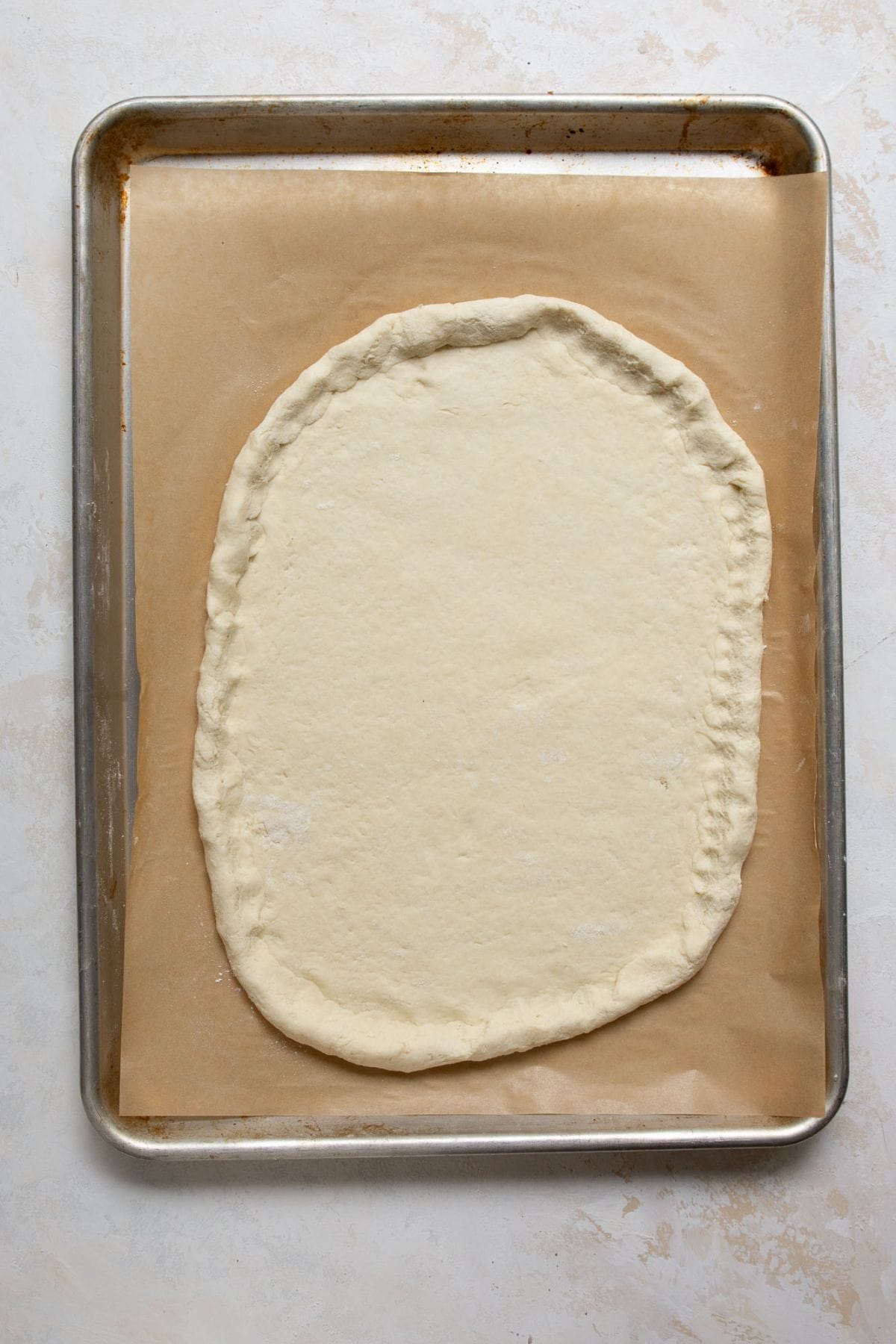 Greek Yogurt Pizza Dough shaped with a crust edge on a parchment-lined baking sheet.
