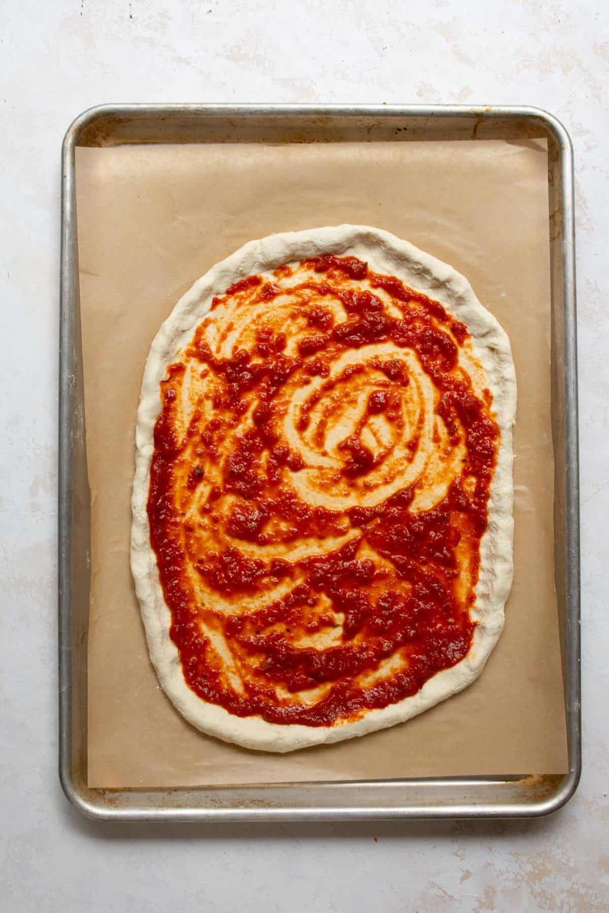 Spreading pizza sauce over Greek Yogurt Pizza Dough before adding toppings.