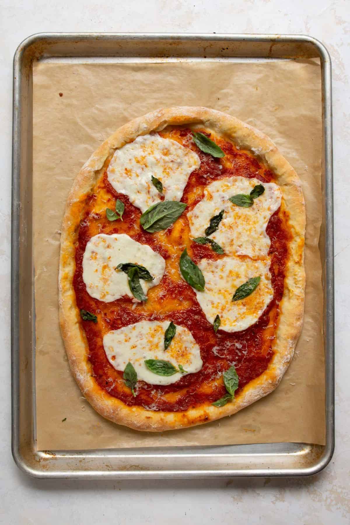 Margherita-style Greek Yogurt Pizza baking on a hot sheet pan until the crust turns golden.