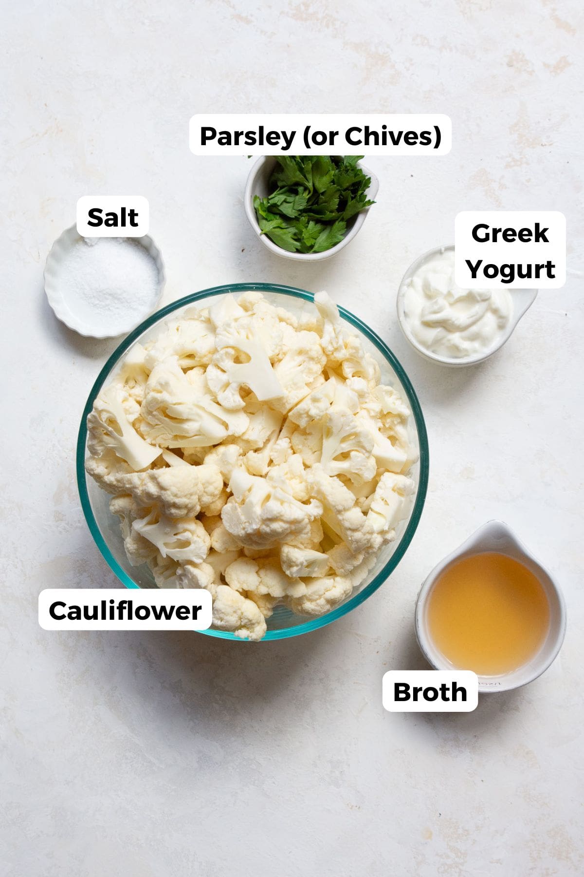 All ingredients for creamy mashed cauliflower with labels: cauliflower florets, plain yogurt, salt, parsley (optional) and broth.