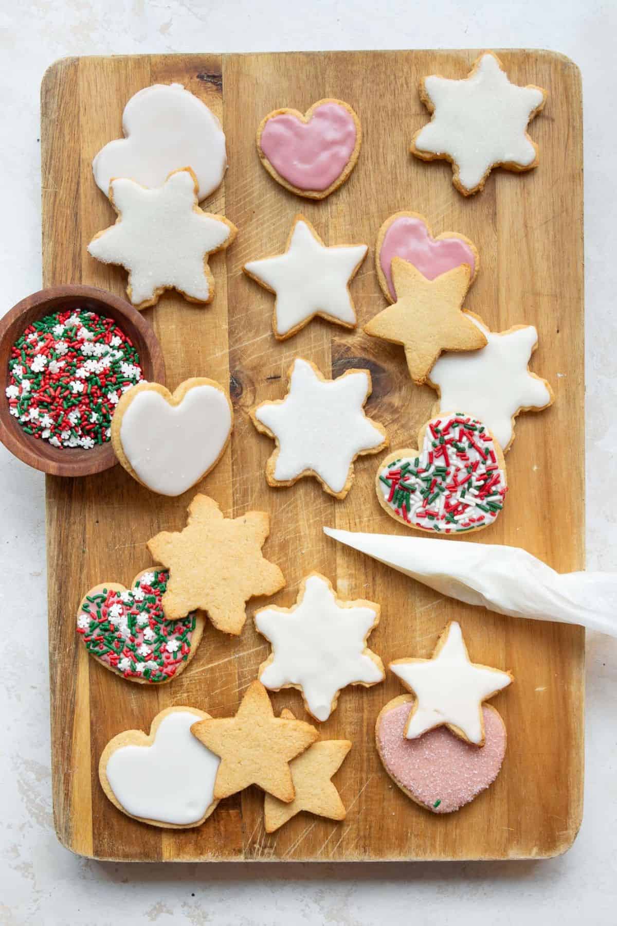 Almond flour Christmas cookies with white and pink icing and holiday sprinkles on a wooden board.
