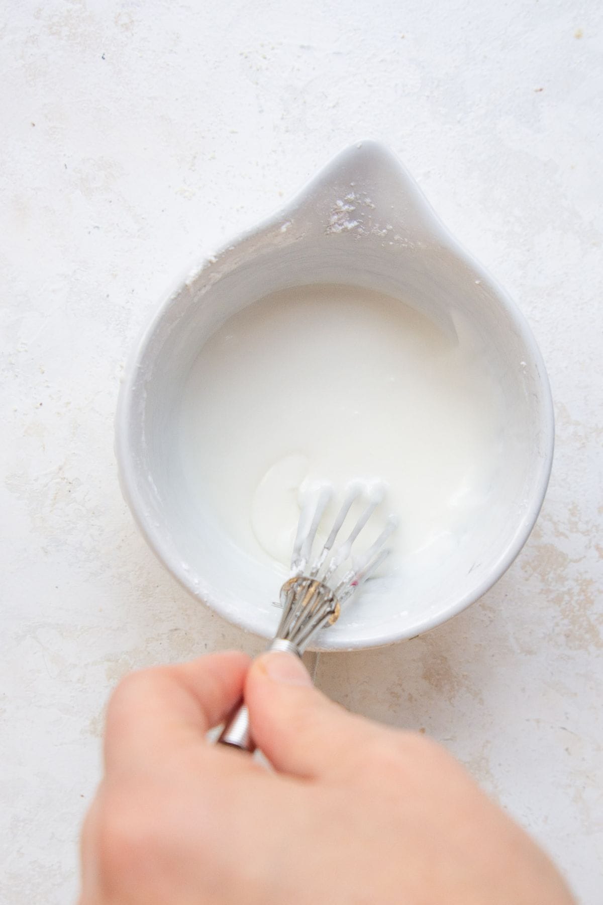 Hand whisking powdered sugar icing in a white bowl.