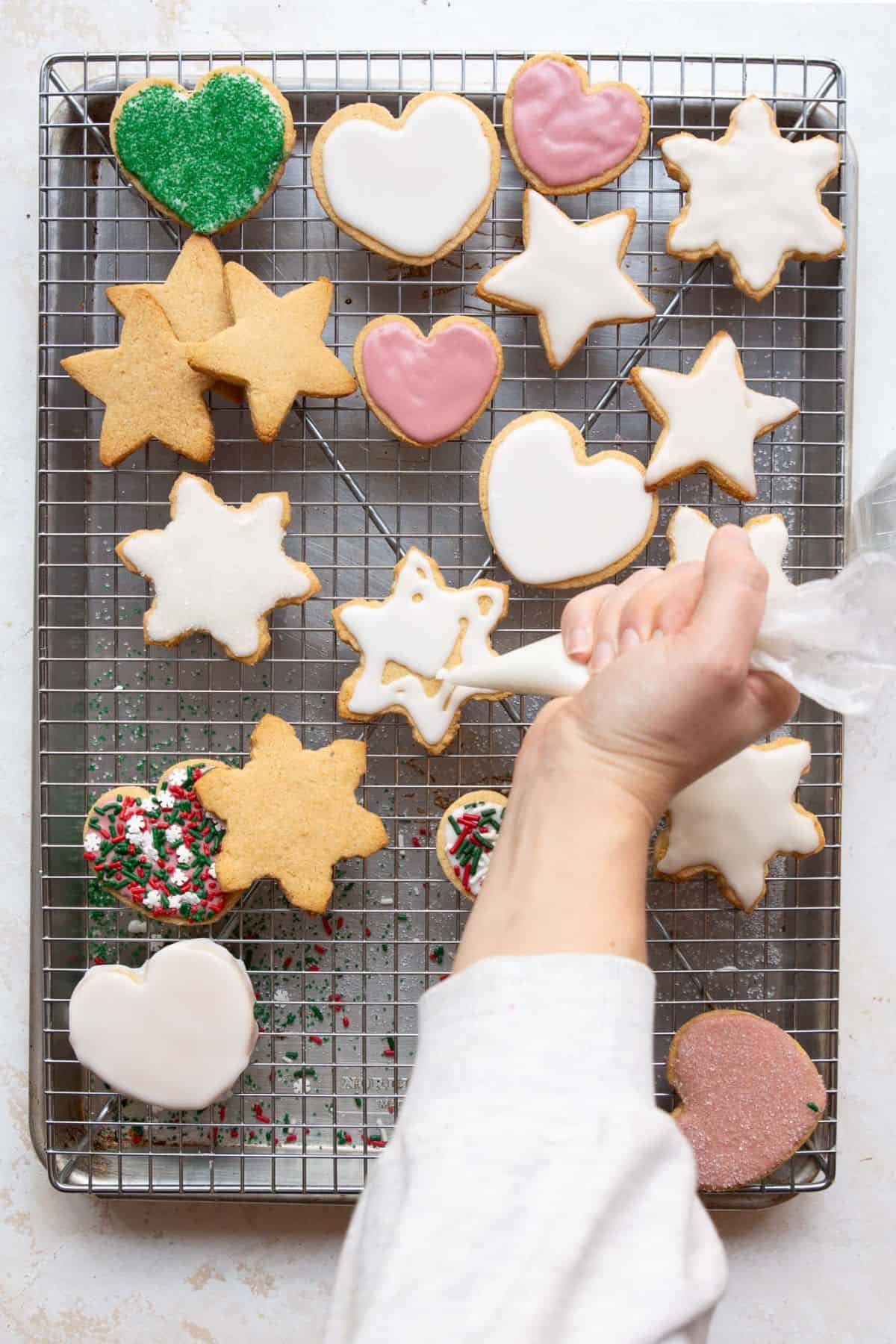Iced star and heart sugar cookies with red and green sprinkles on a wire cooling rack.