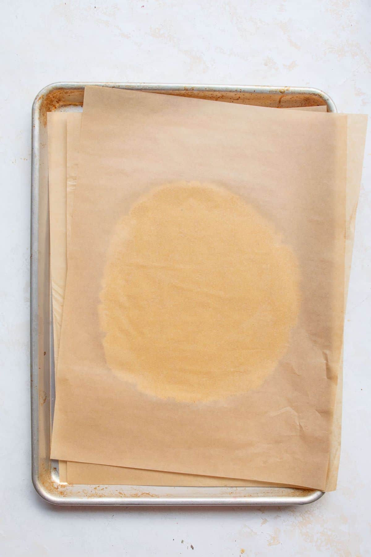 Cookie dough rolled out between two sheets of parchment paper on a baking sheet.