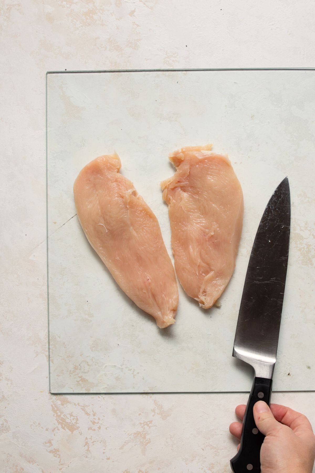 Cutting raw chicken breasts sliced into cutlets.