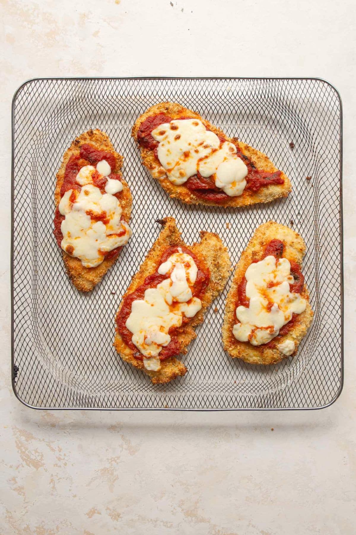 Crispy air fryer chicken parmesan topped with marinara and melted mozzarella in the air fryer basket.