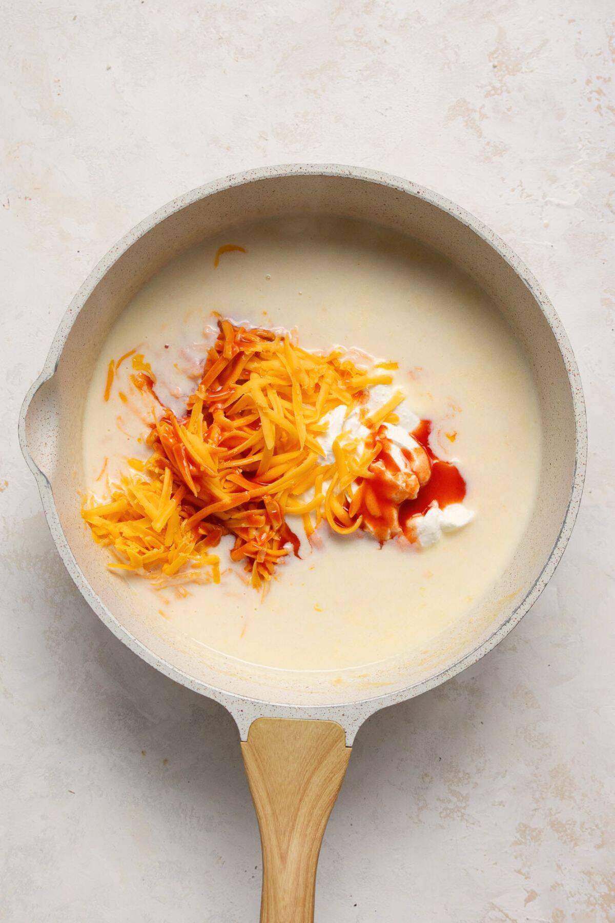 Adding shredded cheddar cheese, blended cottage cheese, and hot sauce to the sauce.