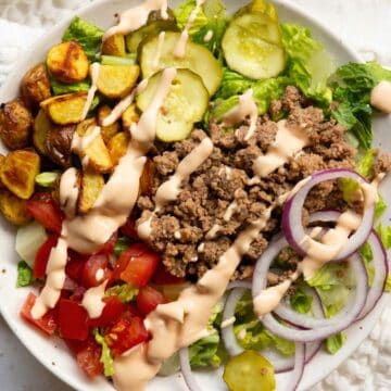 Healthy burger bowl with ground beef, roasted potatoes, romaine, tomatoes, red onion, pickles, and creamy yogurt special sauce.