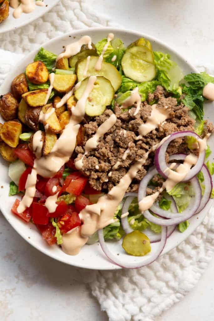 Healthy burger bowl with ground beef, roasted potatoes, romaine, tomatoes, red onion, pickles, and creamy special sauce.