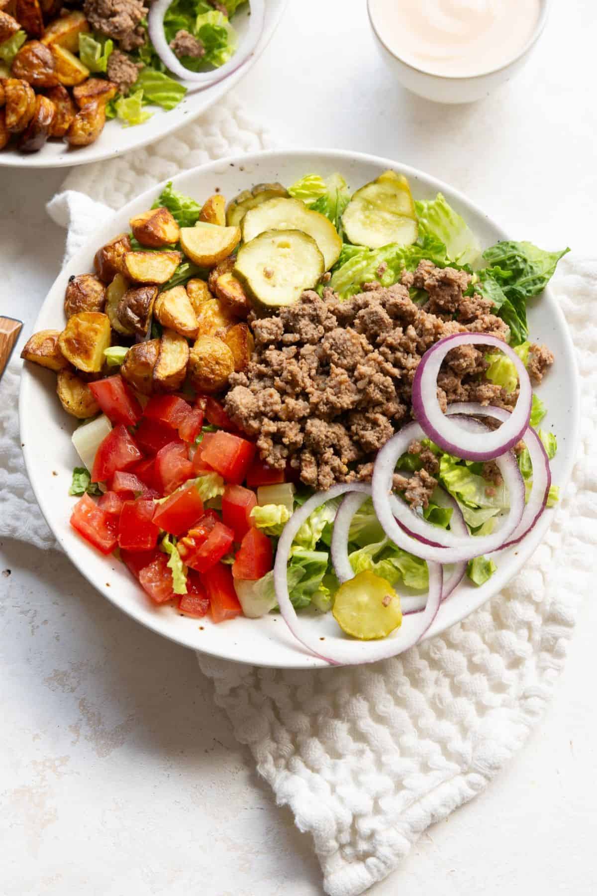 Assembled burger bowl with lettuce, beef, tomatoes, onions, and potatoes.