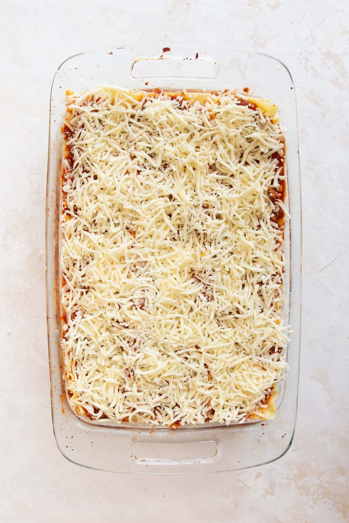Shredded mozzarella sprinkled on top of healthy lasagna before baking.