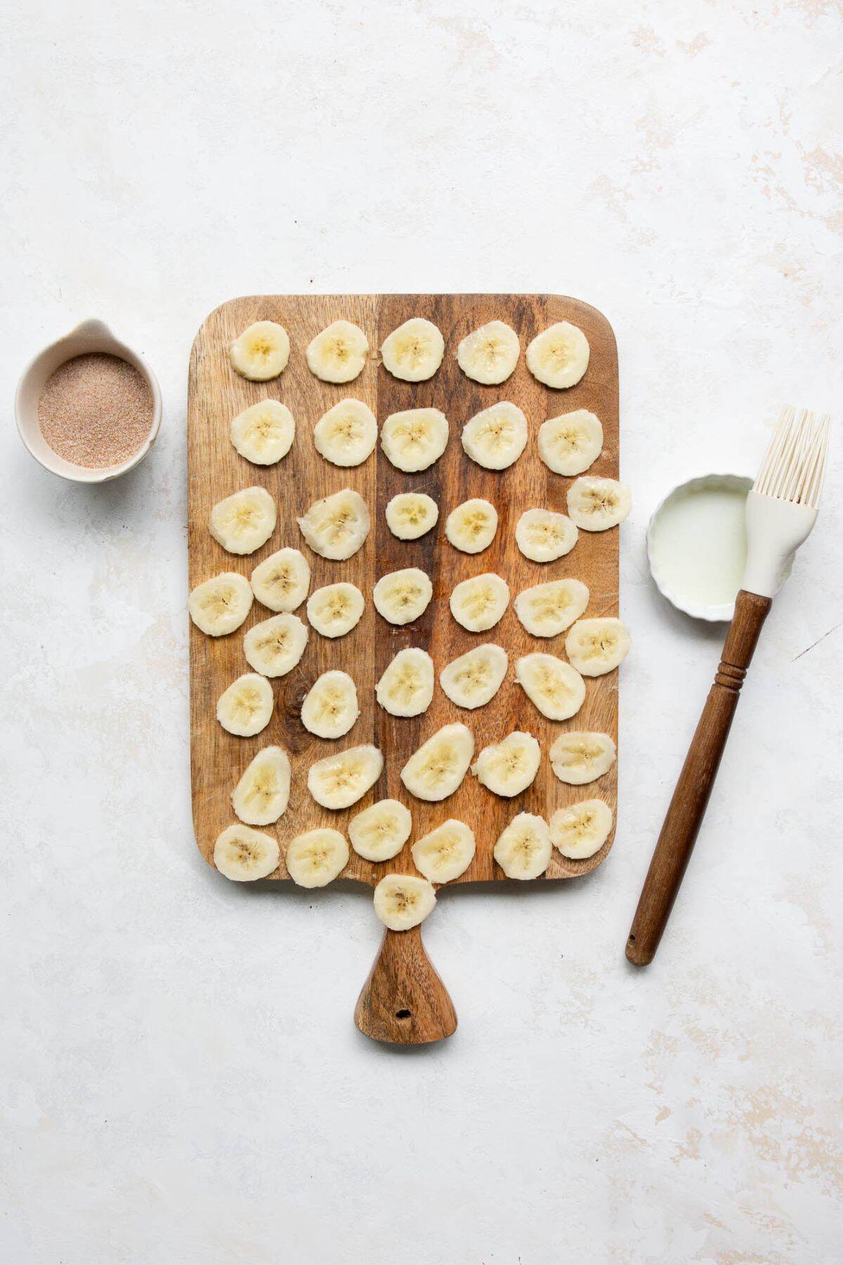 Thinly sliced bananas on a cutting board, brushed with lemon juice before air frying.