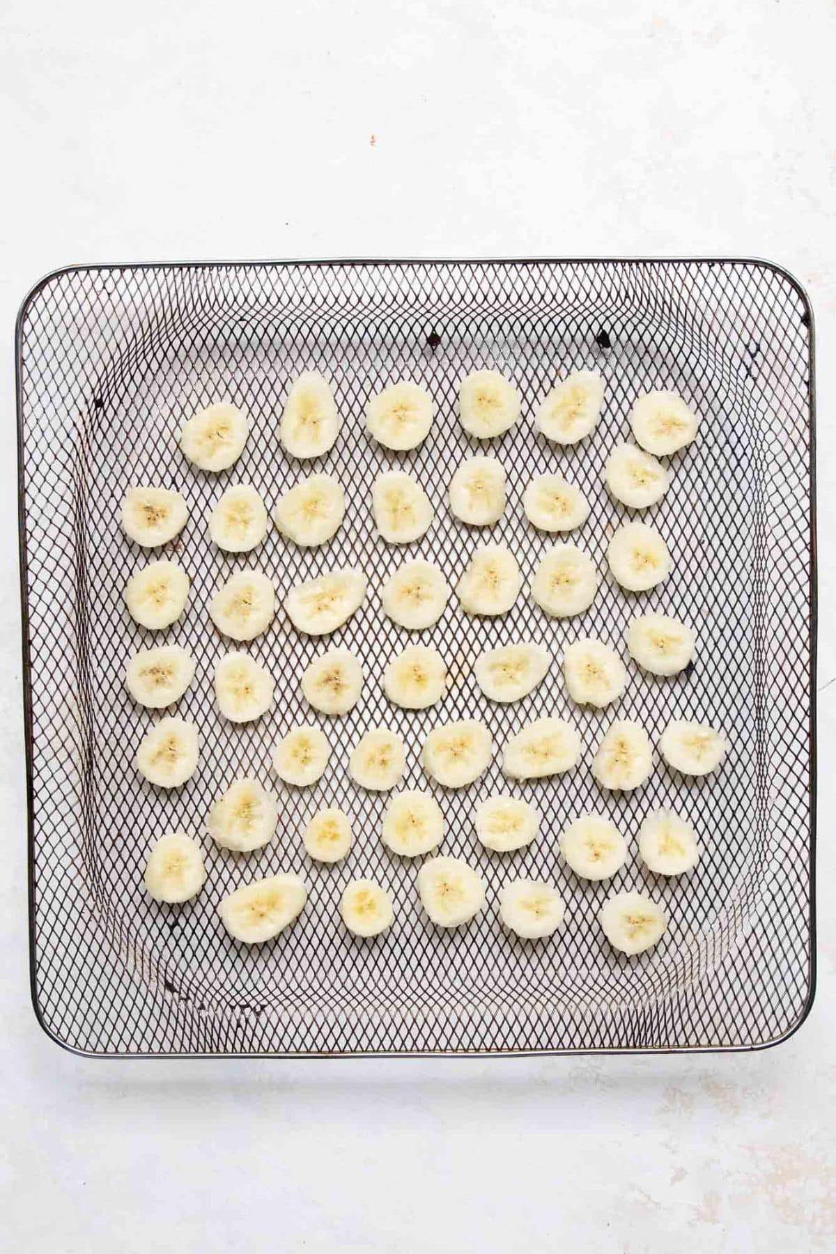 Banana slices arranged in a single layer in an air fryer basket before cooking.
