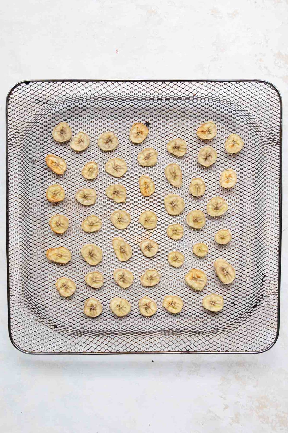 Banana slices starting to dry in the air fryer, lightly golden and shrinking in size.
