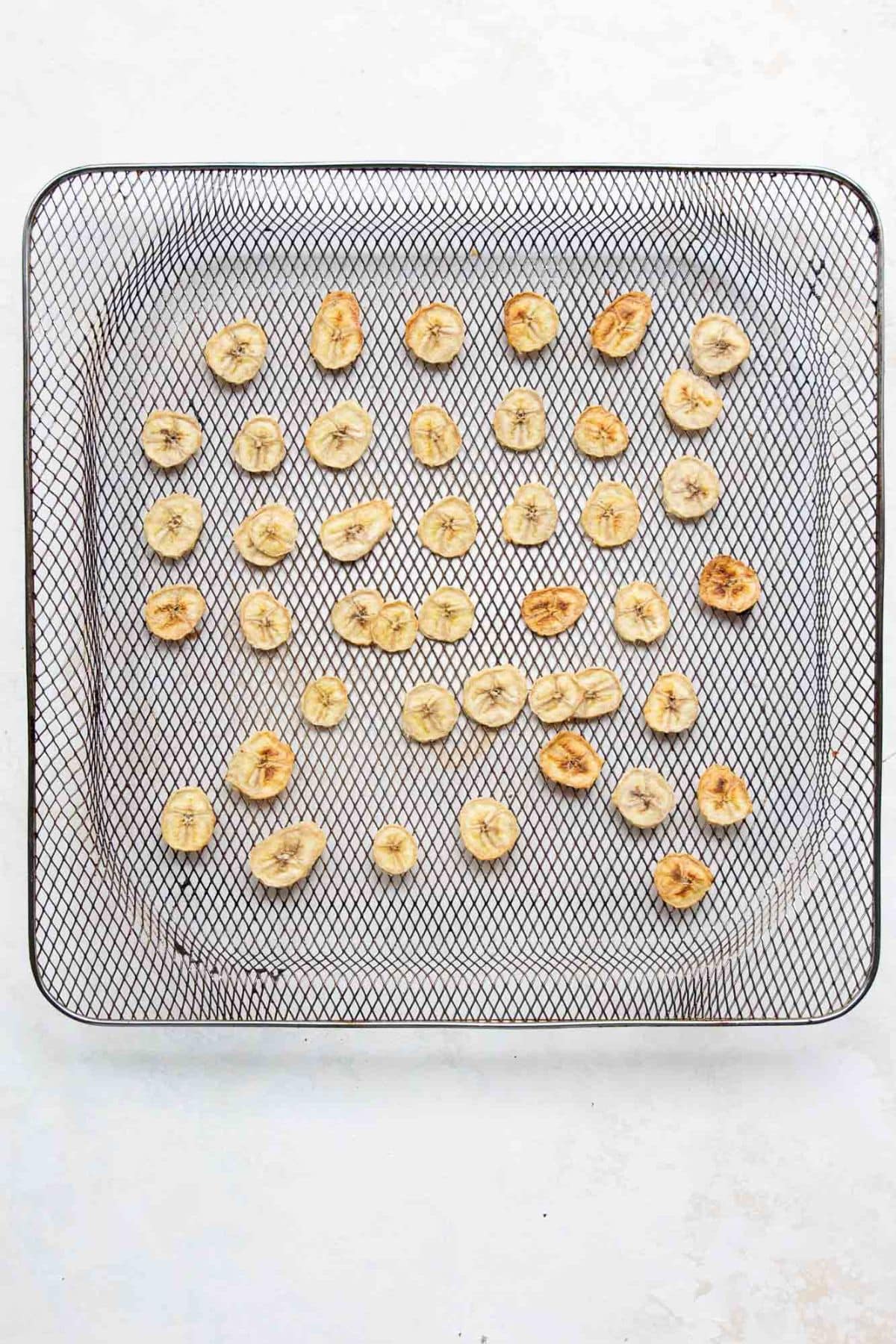 Air fryer banana chips turning golden brown as they finish dehydrating.