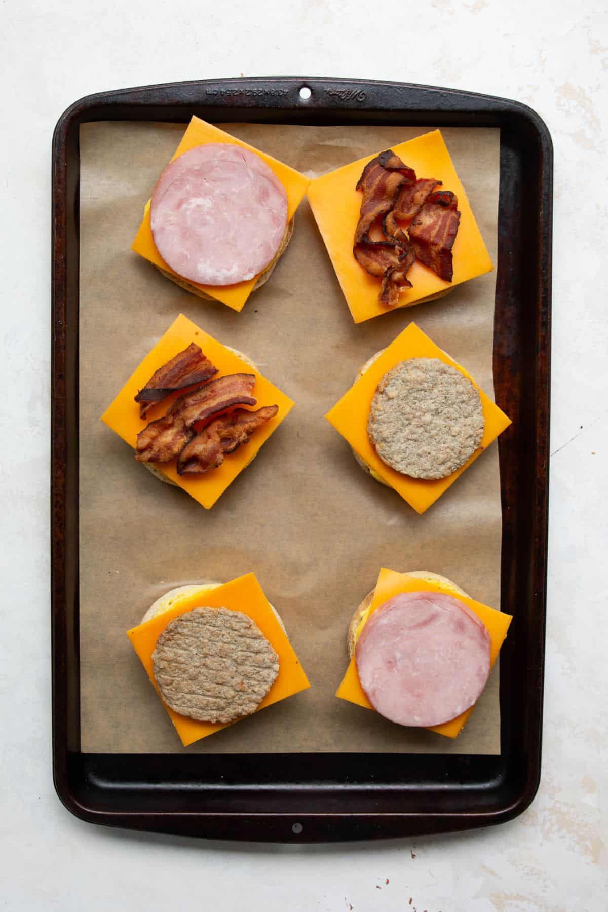 Breakfast sandwiches with egg, cheddar cheese, and sausage, Canadian bacon, or bacon before topping with muffins.