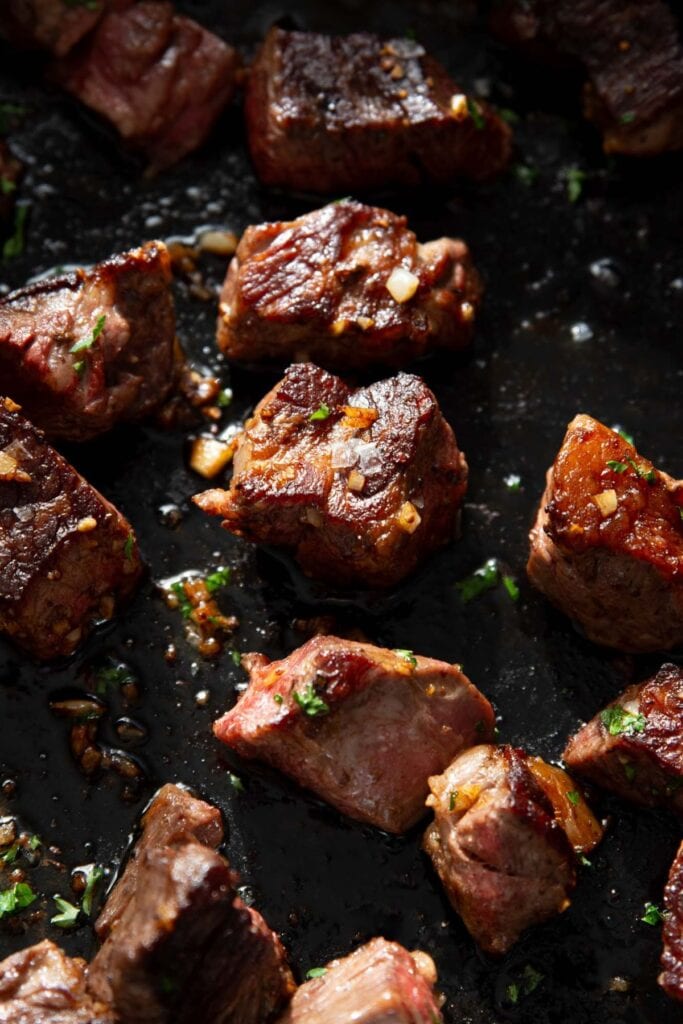 Hot honey garlic butter steak bites seared in a cast iron skillet with fresh parsley.