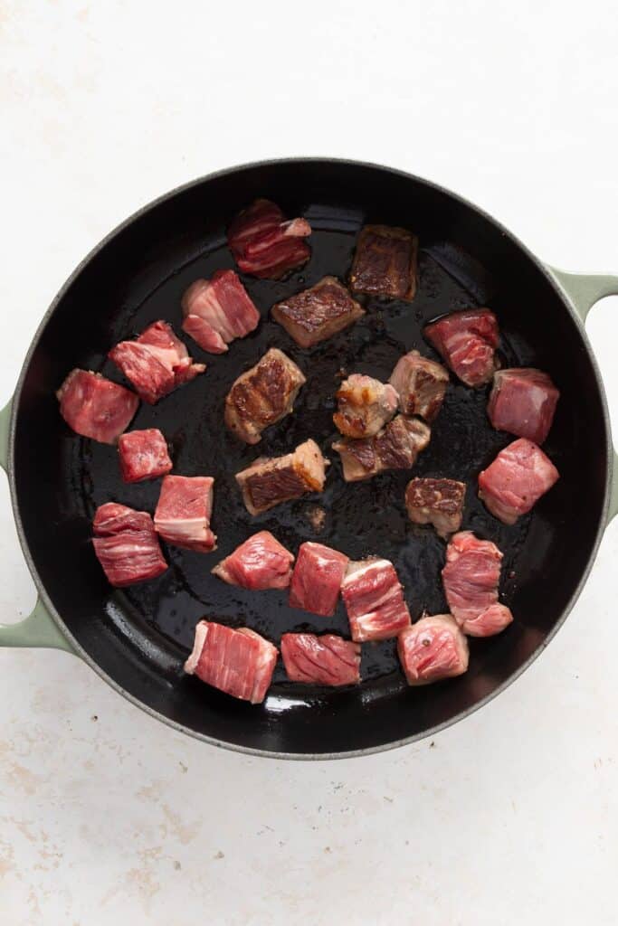 Steak bites searing in a hot cast iron skillet to develop a golden brown crust.