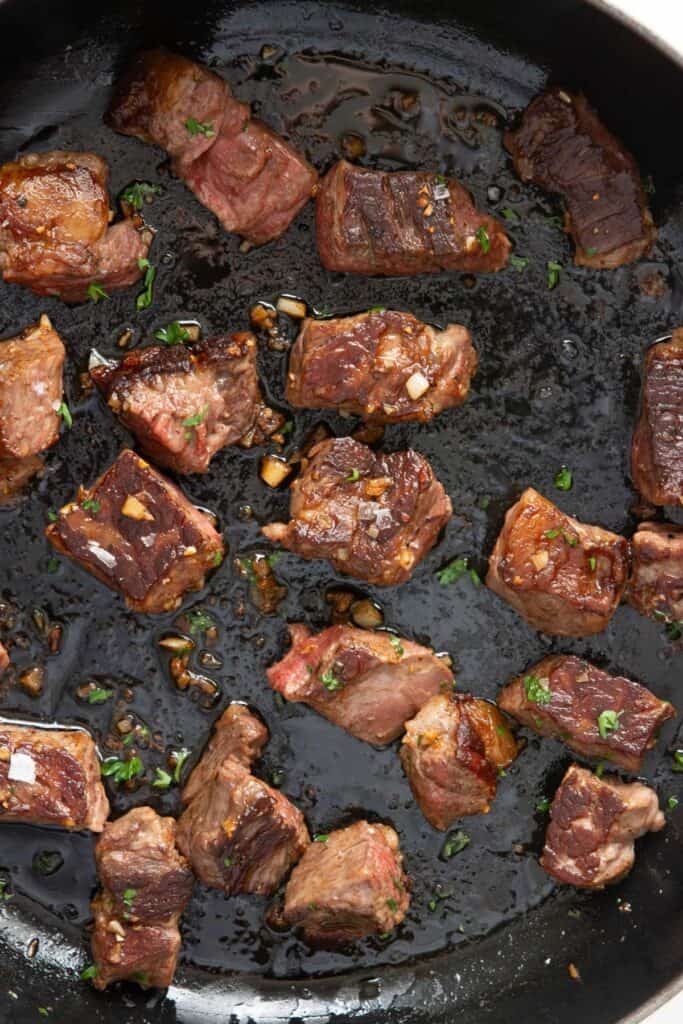 Seared steak bites tossed in pan with parsley, garlic butter sauce, and hot honey.