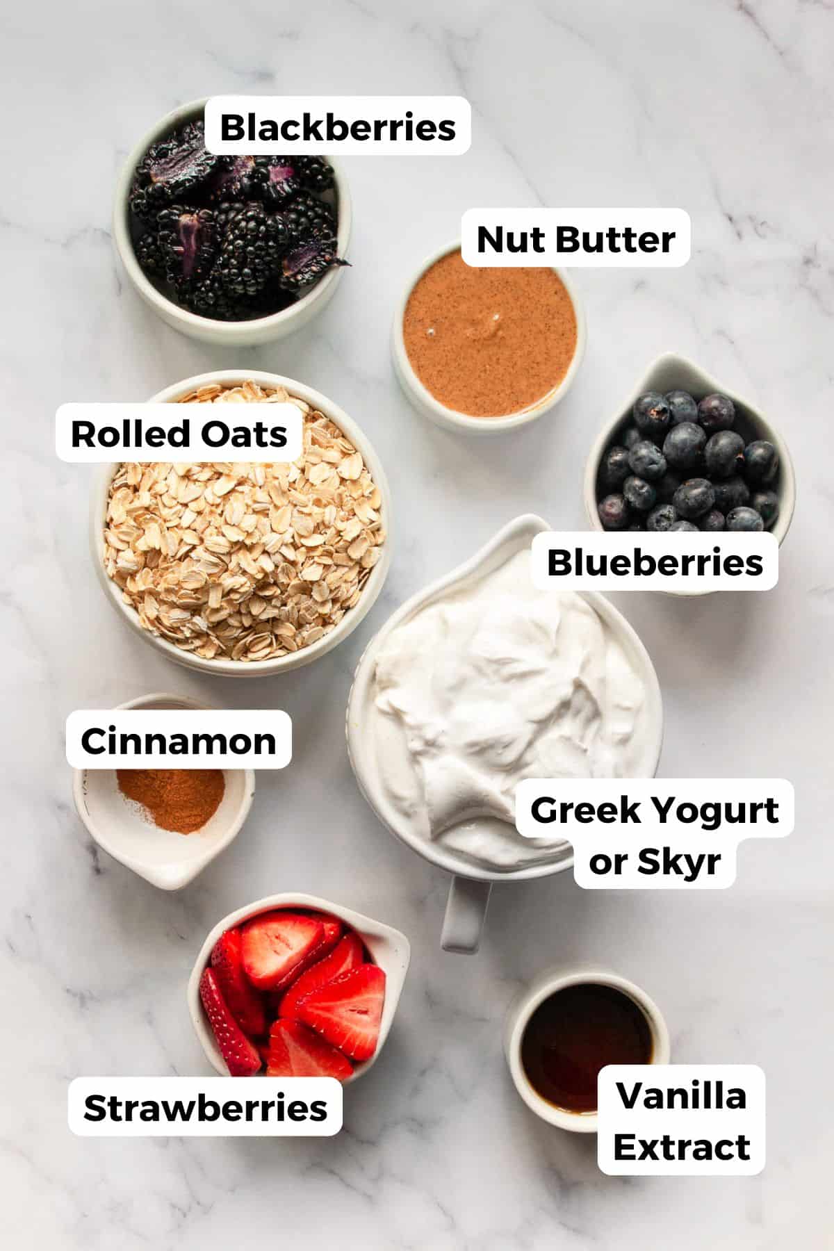Ingredients for frozen yogurt granola bars including Greek yogurt, oats, nut butter, maple syrup, and fresh berries on a marble surface..