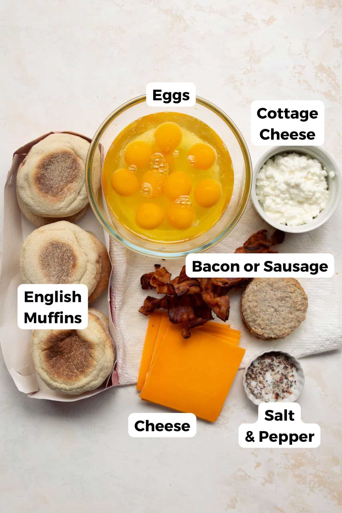 Ingredients for high-protein freezer breakfast sandwiches including eggs, cottage cheese, English muffins, sausage or bacon, cheese, salt, and pepper.