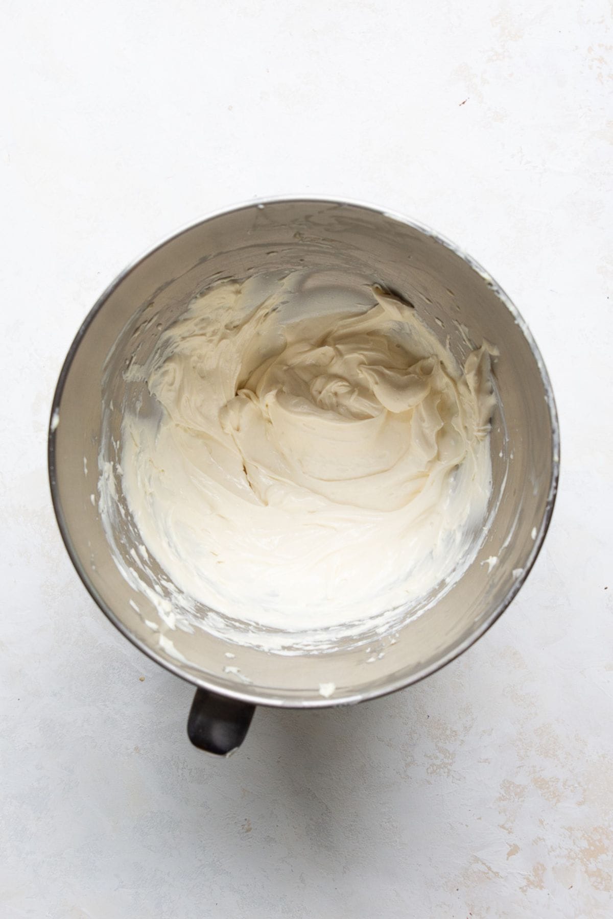 Greek yogurt, maple syrup, and vanilla being added to whipped cream cheese in a mixing bowl.