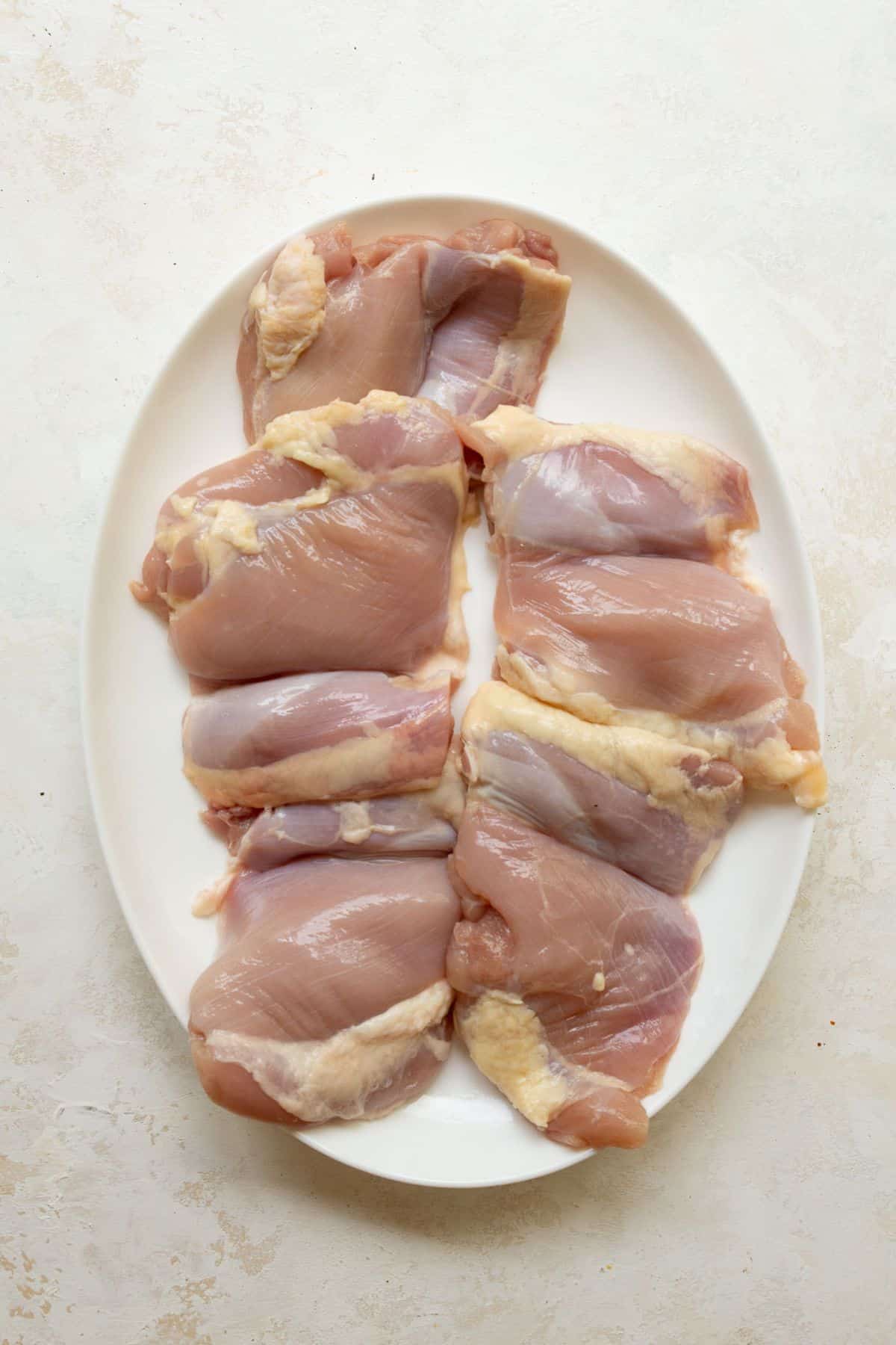 Boneless skinless chicken thighs patted dry with a paper towel on a white plate before seasoning.