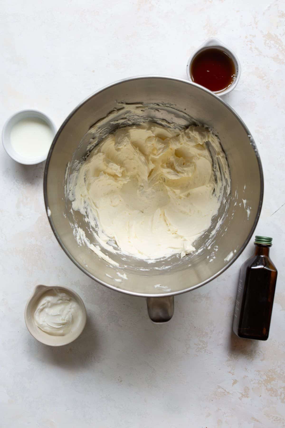 Softened cream cheese being beaten with a hand mixer in a bowl until smooth and lump-free.