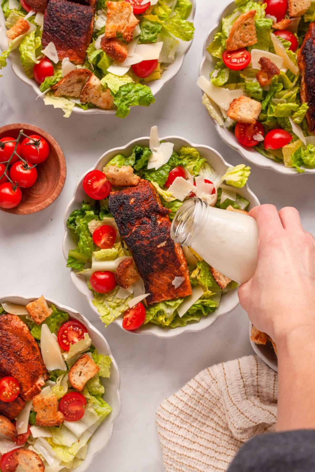 Pouring healthy Caesar dressing on top of salmon Caesar salad.