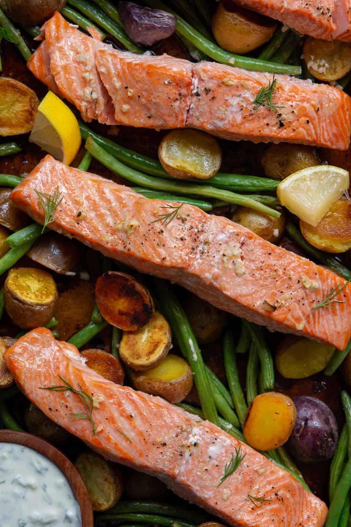 Flaky baked salmon with crispy lemon garlic potatoes on a sheet pan.