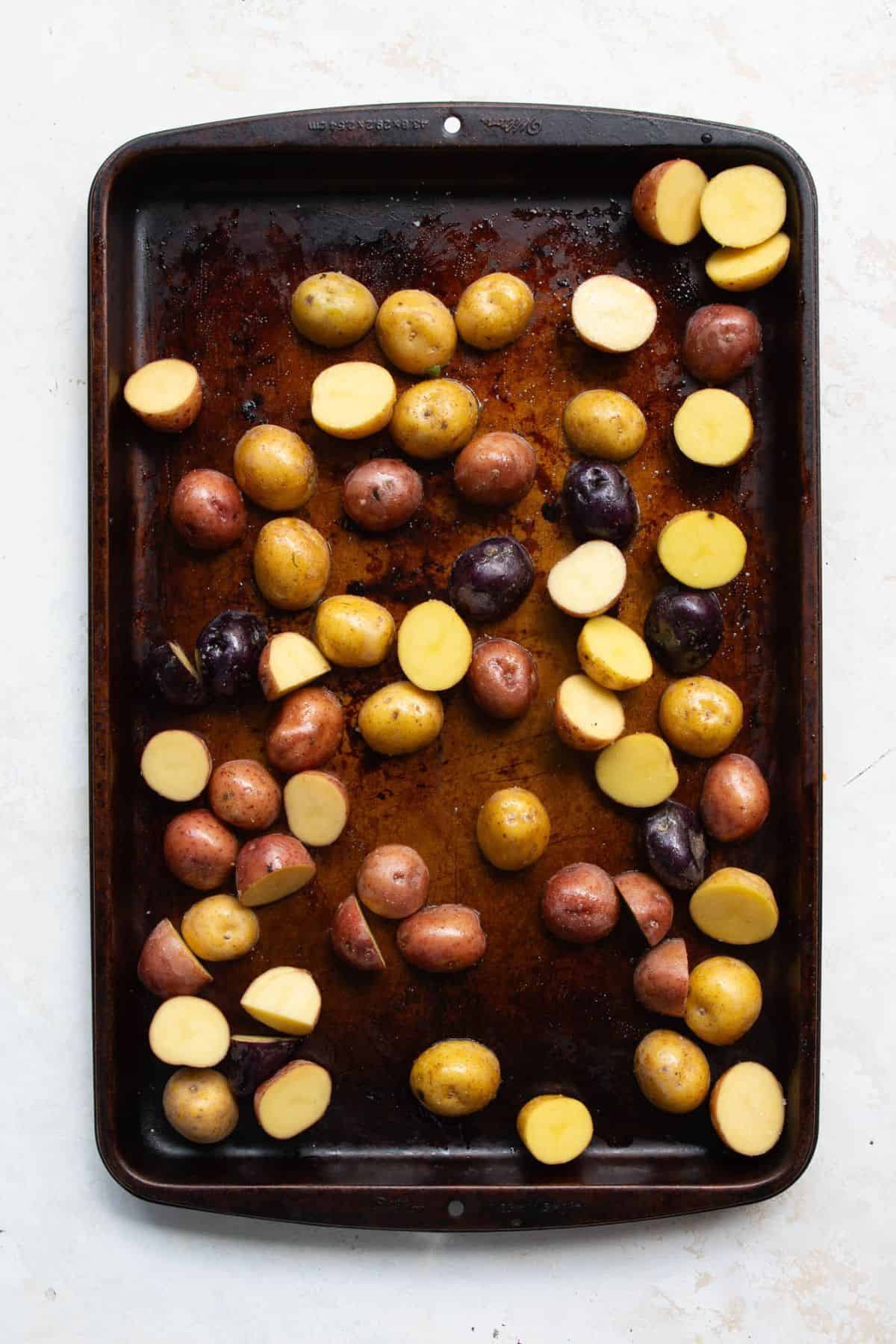 Yukon gold potatoes seasoned with olive oil on a baking sheet before roasting.