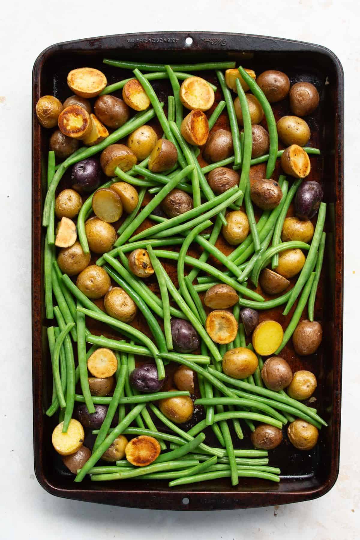 Green beans added to roasted potatoes on a sheet pan.