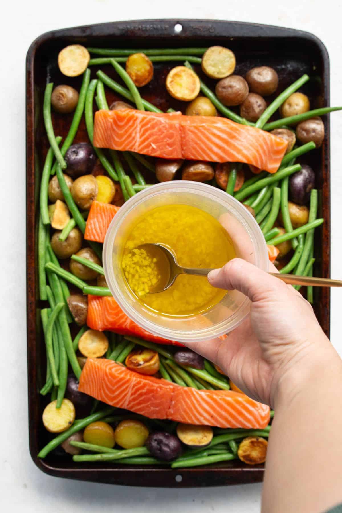Lemon garlic oil being drizzled over salmon and vegetables.