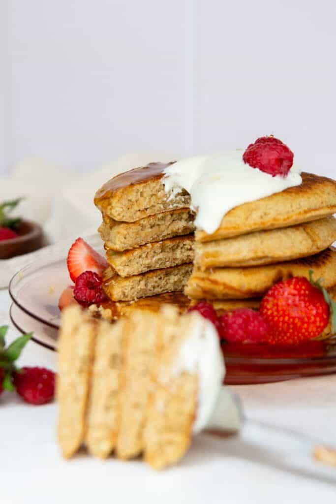 Stack of fluffy oat flour pancakes cut open to show the soft tender center, topped with Greek yogurt and fresh raspberries.