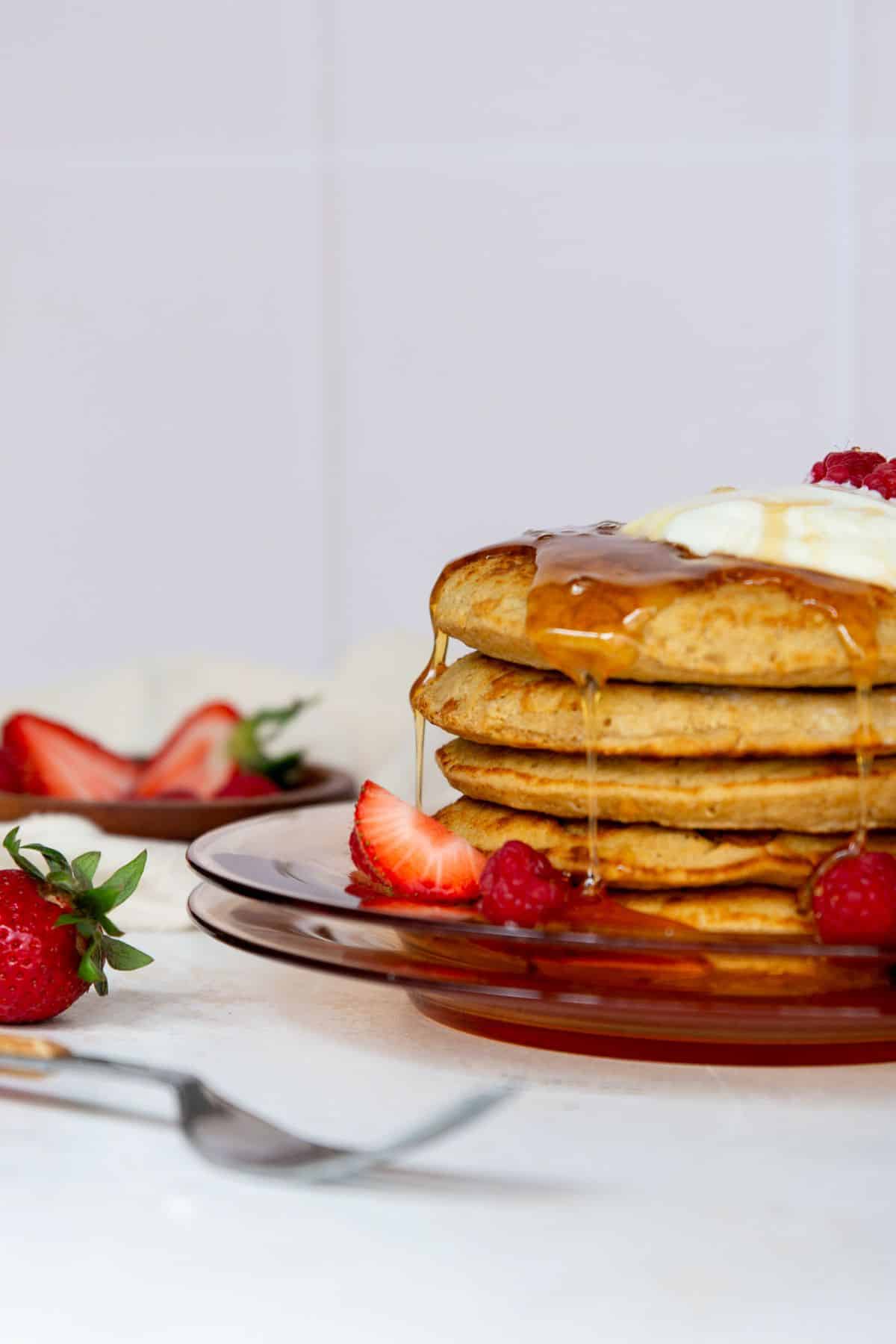 Stack of oat flour pancakes with maple syrup and fresh berries.