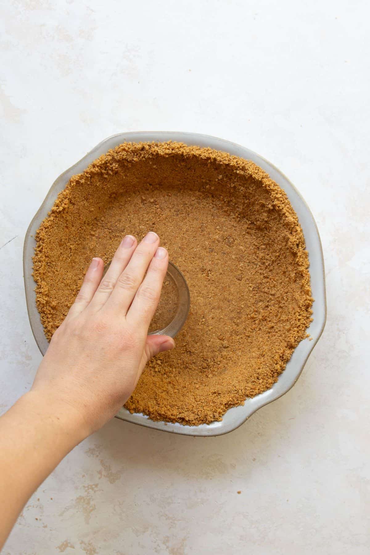 Pressing gluten-free graham cracker crust into a pie dish with the bottom of a glass.